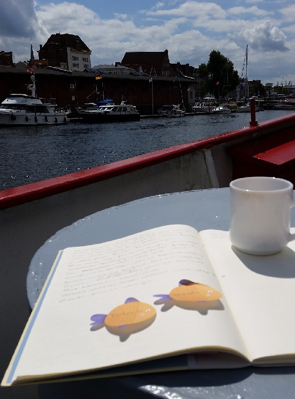 aufgeschlagene Schreibkladde, dahinter ein Fluss und Lübeck